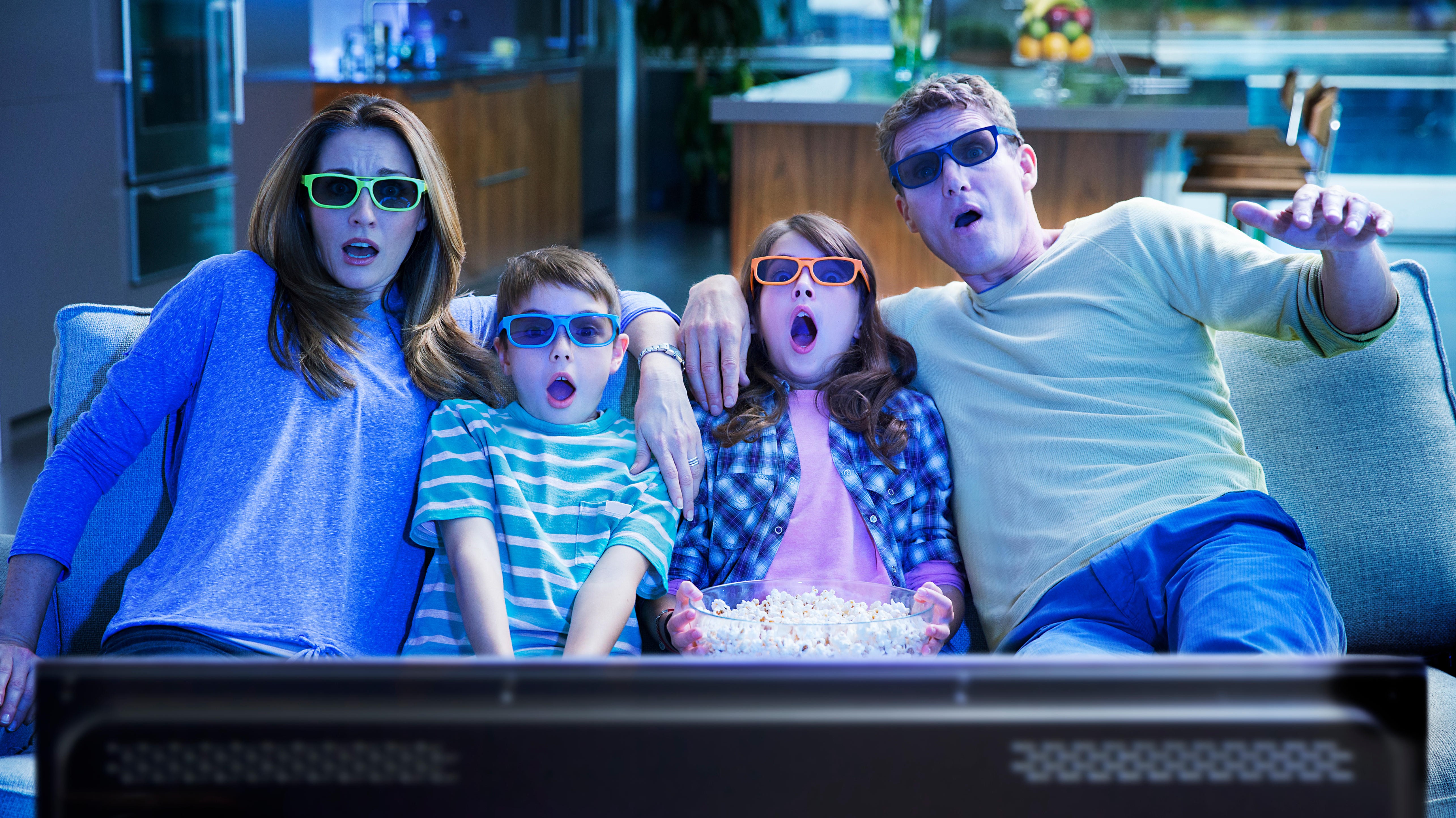 A family of four watches TV while wearing 3D glasses.
