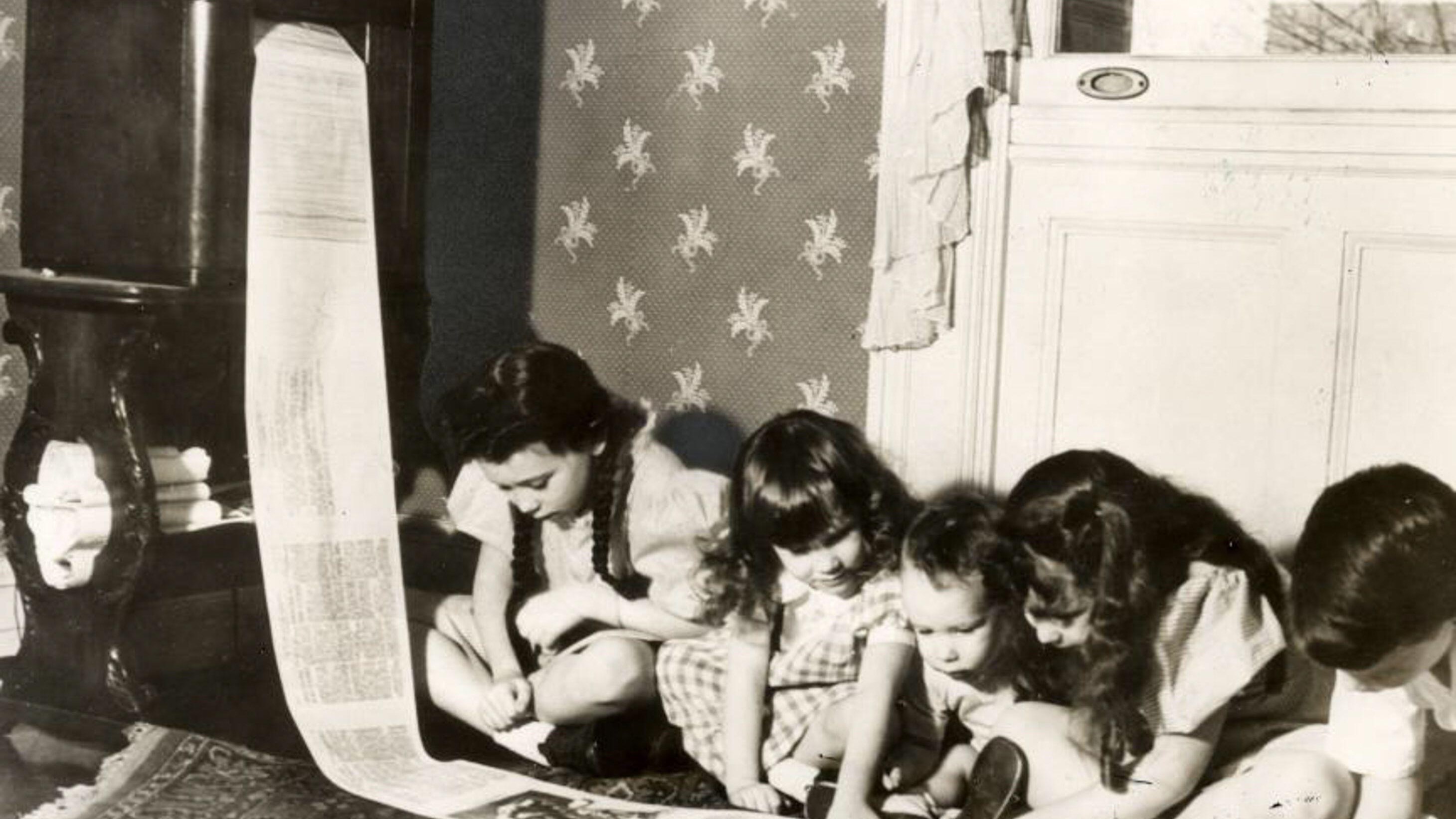 Children kneel on the floor to read a radio newspaper that is being printed.