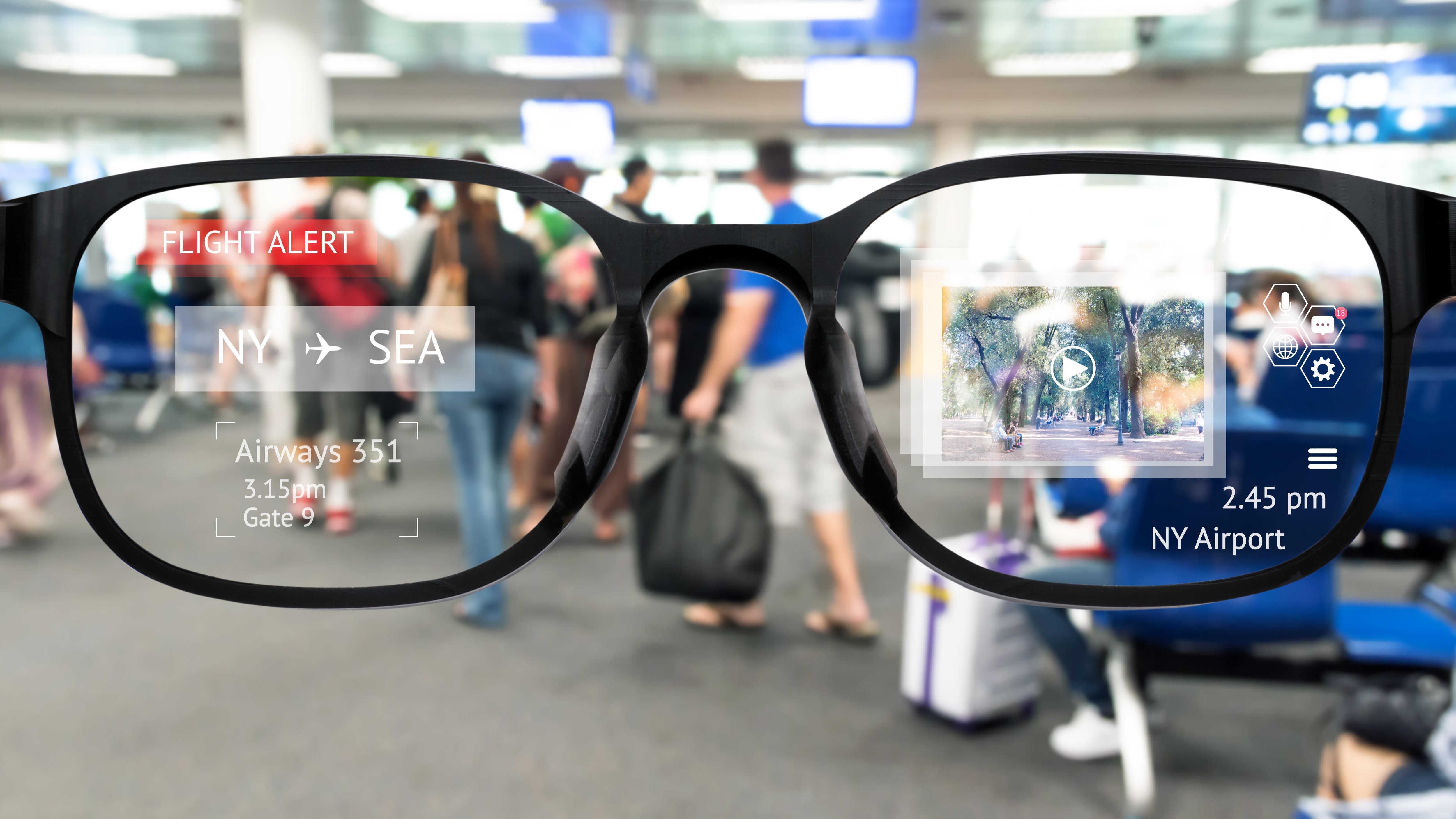 A pair of augmented reality glasses held up against an airport lounge backdrop.