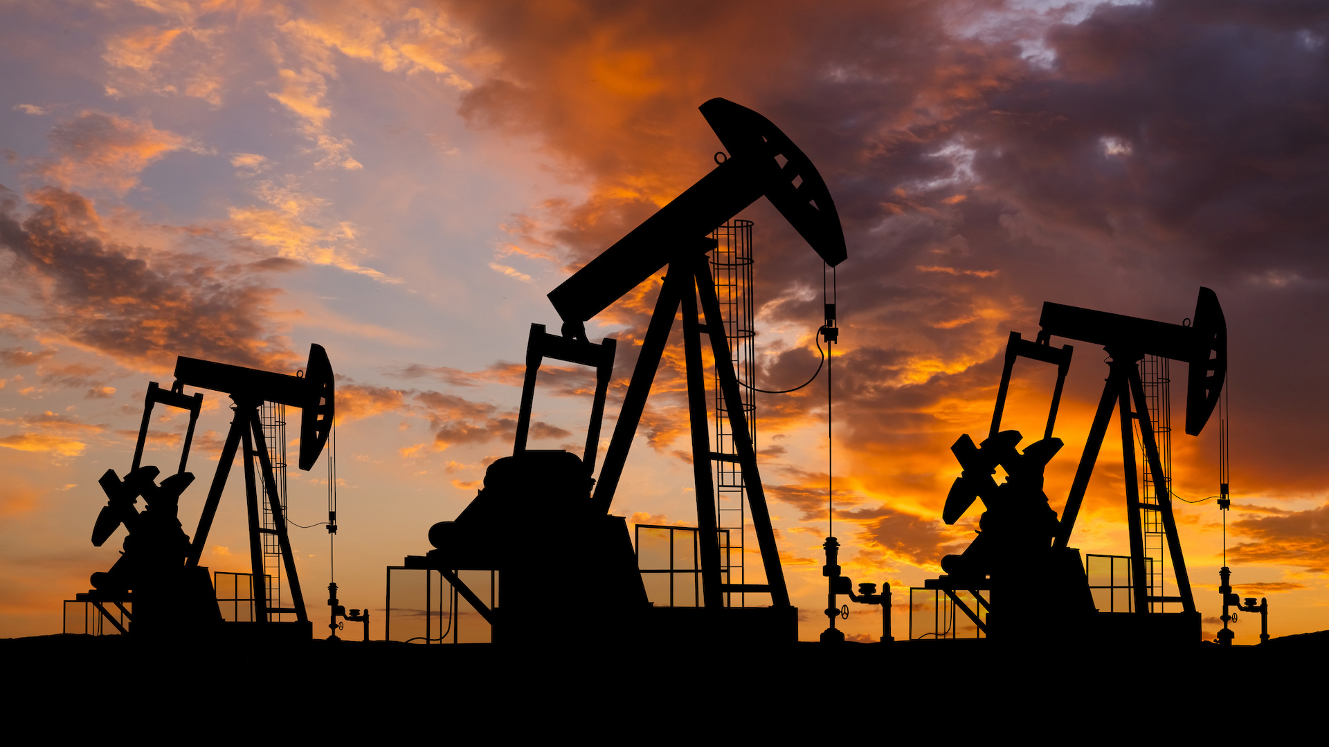 A photograph of the silhouettes of oil derricks on a sunset