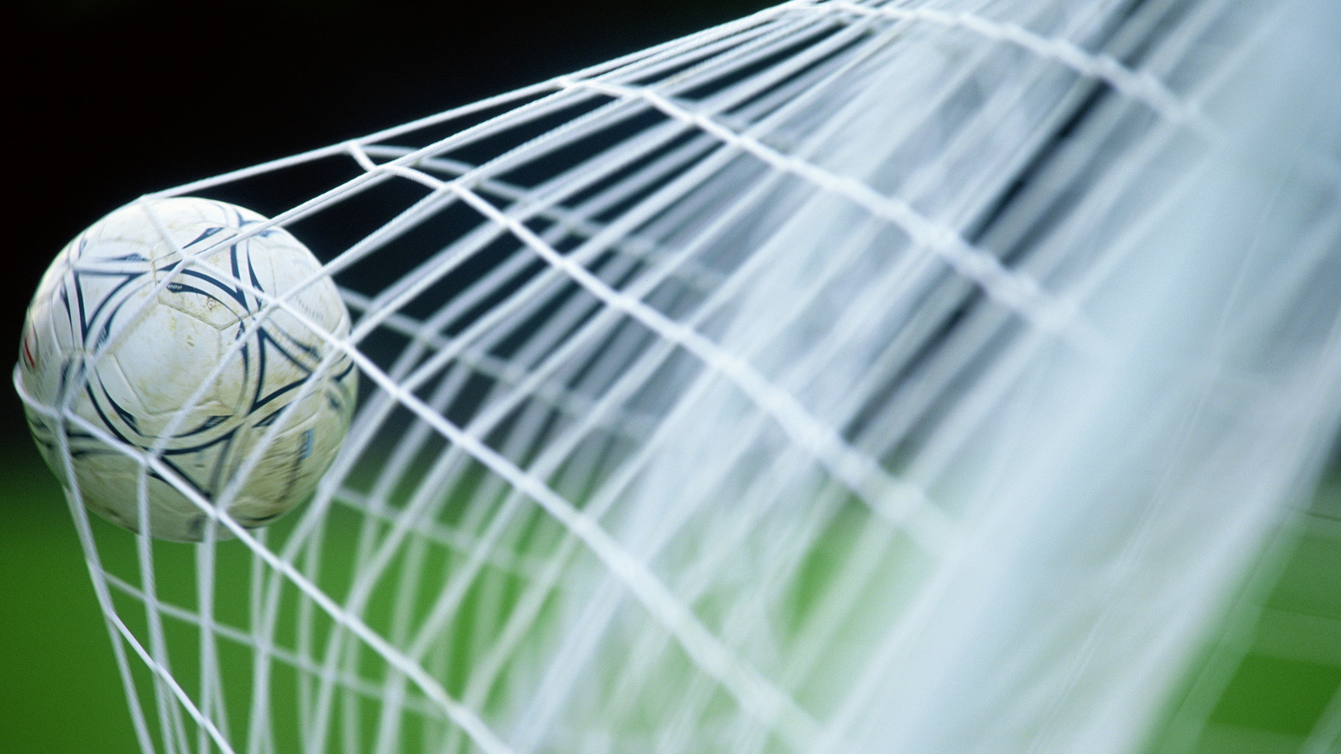 photo of a soccer ball hitting the back of a net on a green field