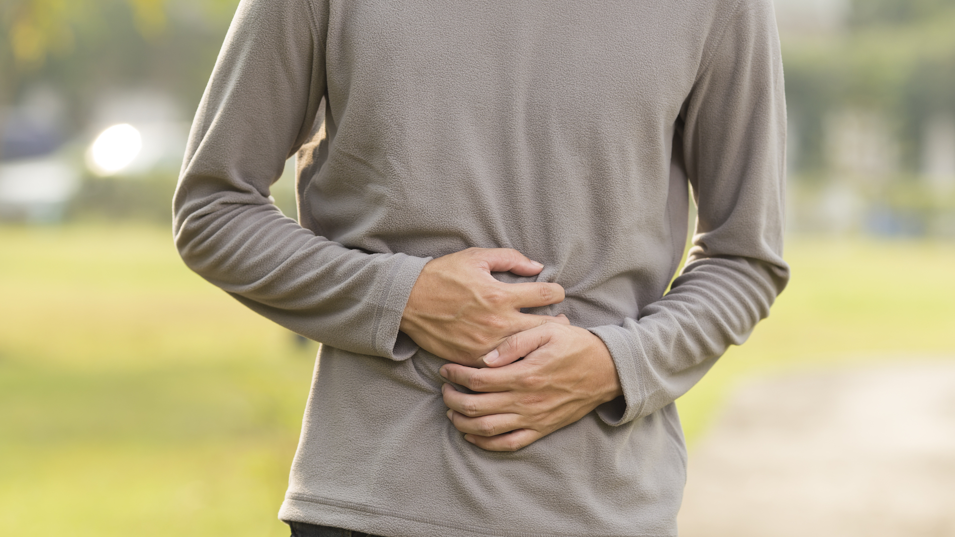 Photo of a man clutching his stomach while standing outside