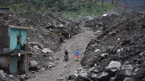 Getty Images A street carved through huge piles of rock and ash, with a few ruined houses