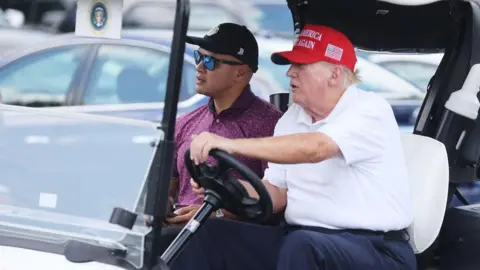 Getty Images  Donald Trump drives a golf cart accompanied by aide Walt Nauta