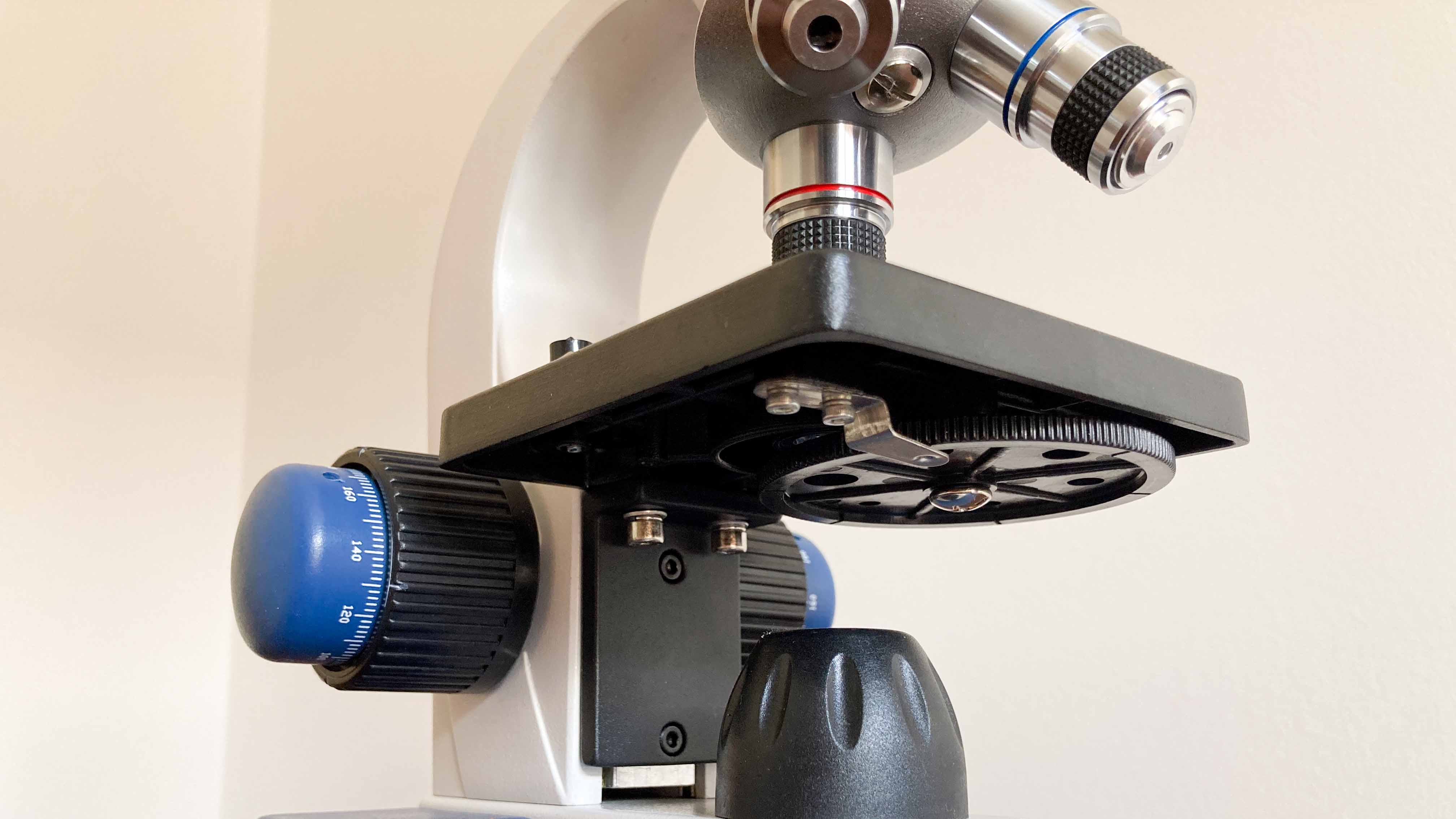 A close-up view displaying the microscope's single lens condenser, diaphragm, LED adjustment control, sturdy stage, coaxial coarse and fine focusing knobs and objective lenses