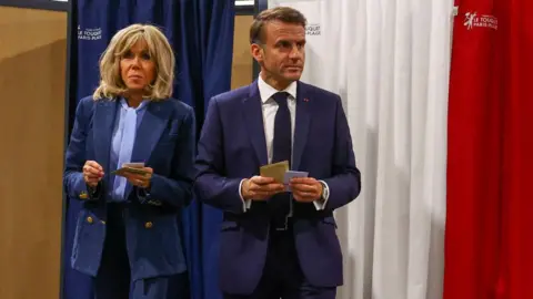 AFP France's President Emmanuel Macron (R) and his wife Brigitte Macron (L) exit a polling booth, adorned with curtains displaying the colors of the flag of France, before casting their ballot for the European Parliament election at a polling station in Le Touquet, northern France on June 9, 2024