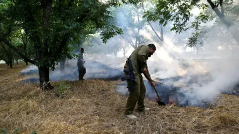 Getty Images Israeli first responders use shovels to put out flames near Kiryat Shmona on 4 June 2024