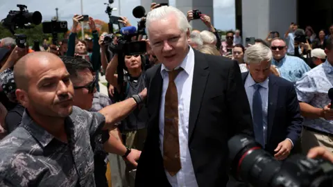 Reuters Julian Assange is led through a group of journalists outside court