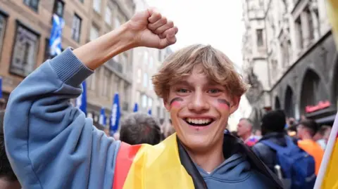 PA Media A young man wearing a German flag and with the German flag on his cheeks looks happy in Munich, 13 June 2024