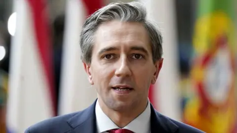 Getty Simon Harris looking at the camera wearing a navy blazer, white shirt and red tie