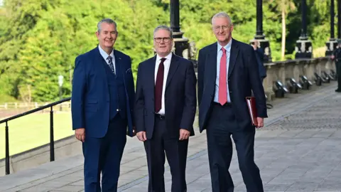 Pacemaker Edwin Poots, Sir Keir Starmer and Hilary Benn - Three men in suits stand at the top of the steps of Stormont