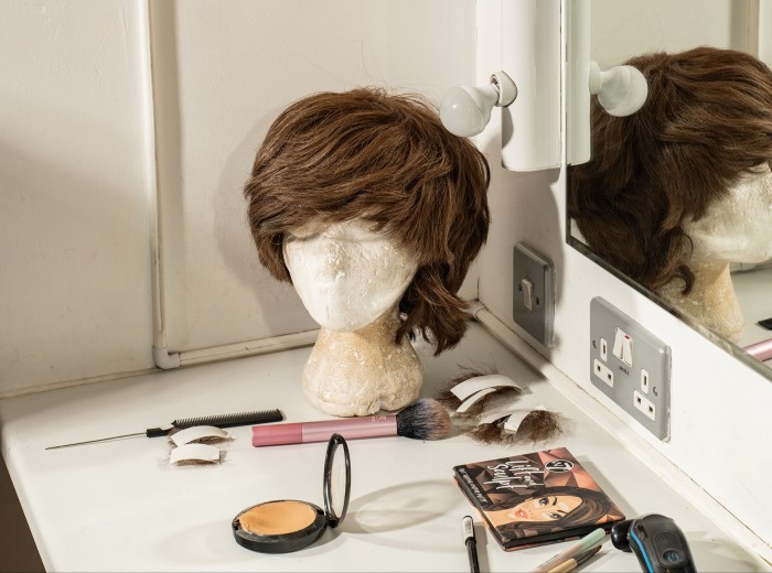 A dressing room containing make-up and a wig on a stand