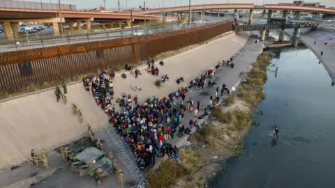 Getty Images Texas officials stand near razor wire as migrants cross water