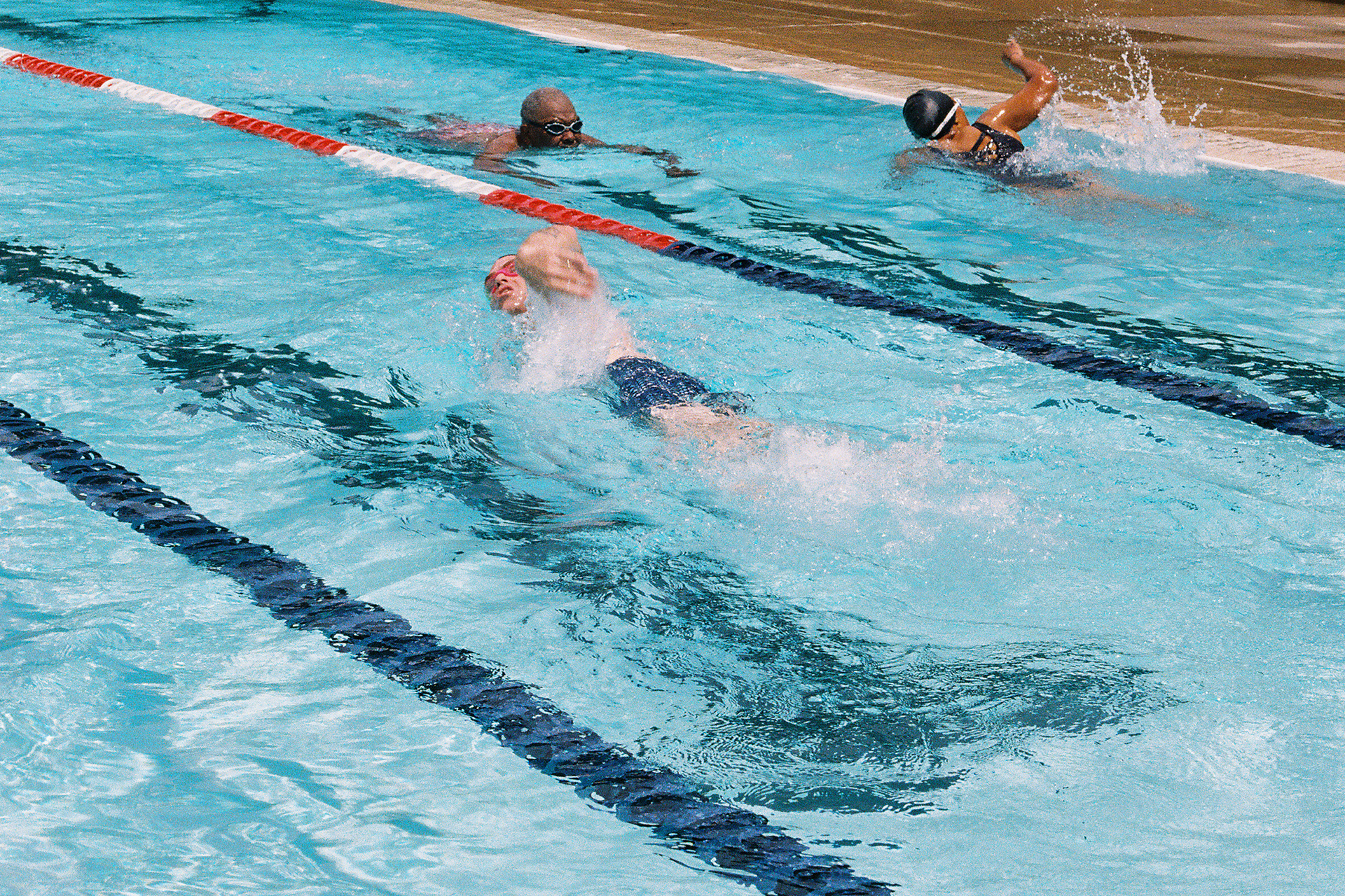 Three people swimming in lanes of a public pool