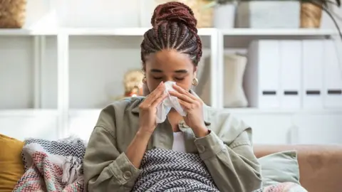 Getty Images Woman sat under a blanket and blowing her nose