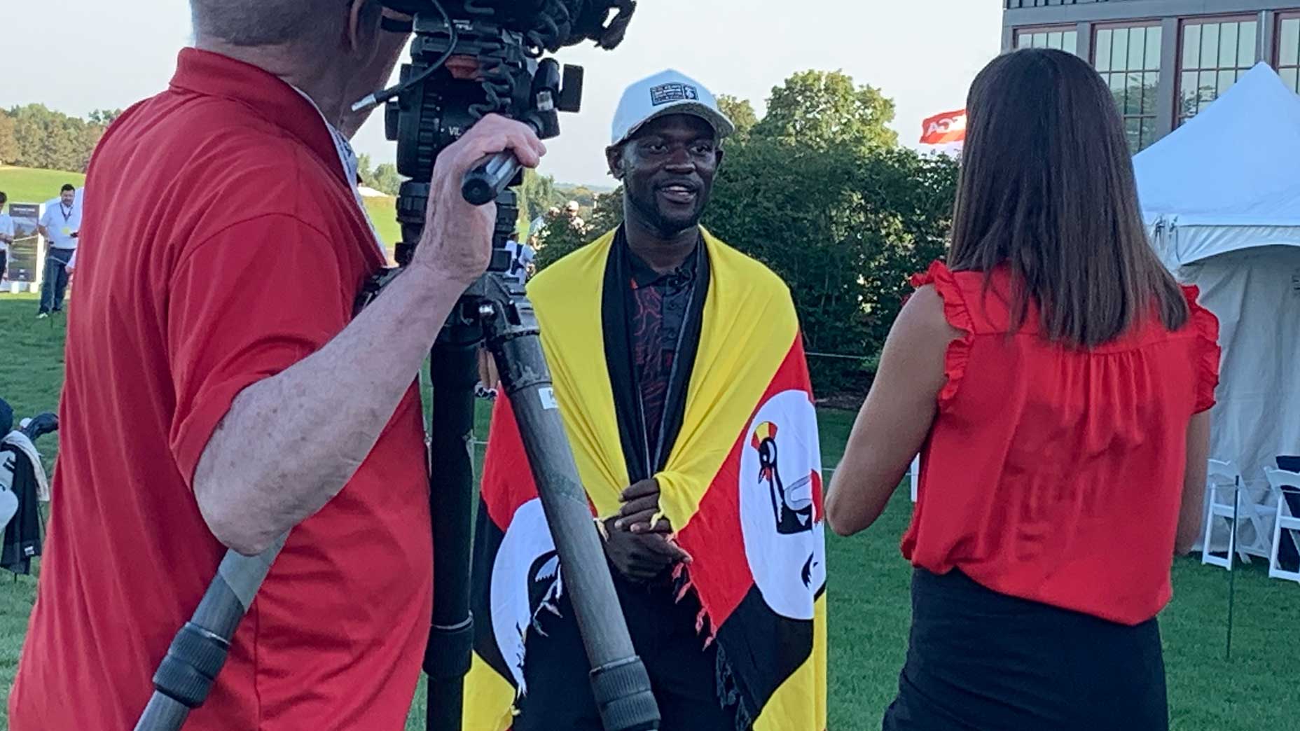 Godfrey Nsubuga, with the Uganda flag, after his round at Hazeltine on Monday.