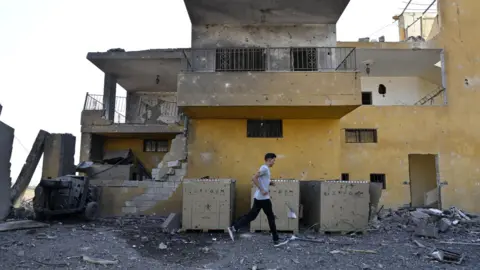 EPA A man walks past a building damaged in a reported Israeli air strike in Nabi Sheet, Lebanon (21 August 2024)