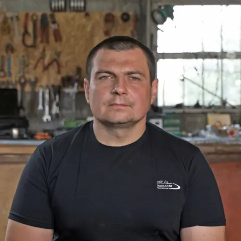 Dmytro Herasymenko sits in a garage in front of a wall of tools