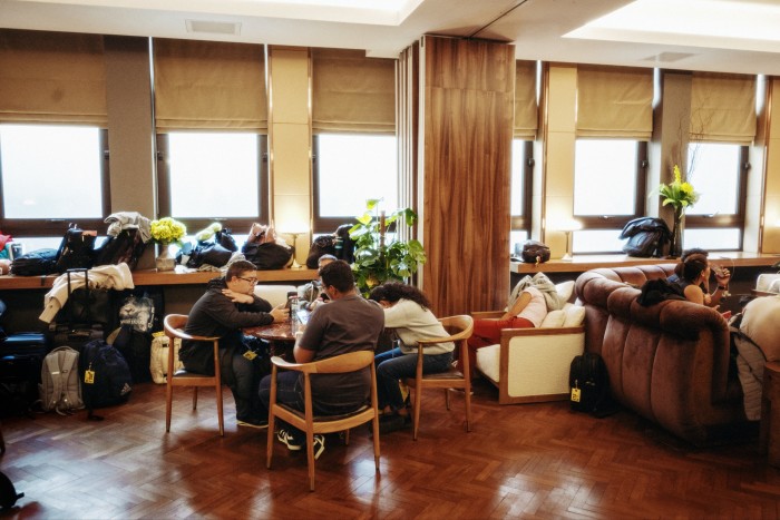 Tired orchestra members sit around a hotel lobby with their luggage and instruments