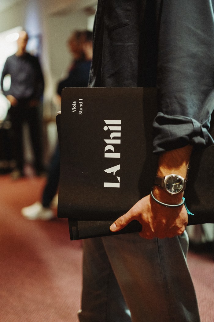 View of a man carrying an orchestral score in a folder that reads “LA Phil”