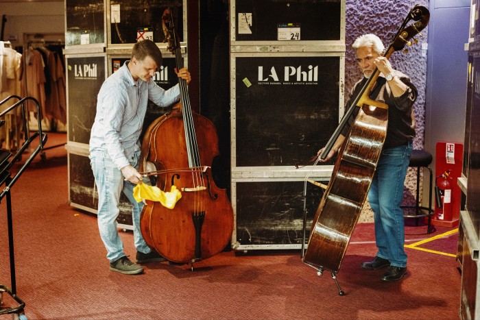 Two double bass players playing backstage, surrounded by large flight cases