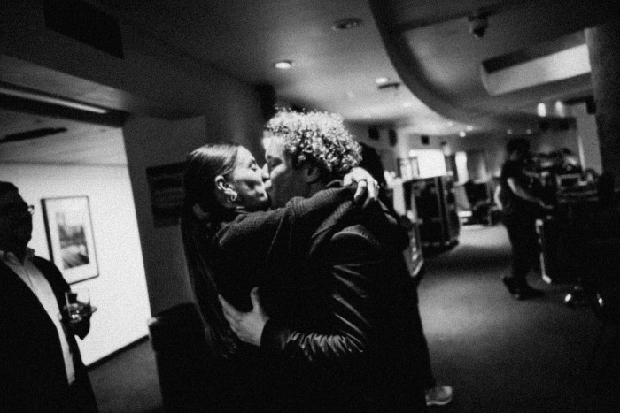 A man and a woman passionately embracing and kissing backstage