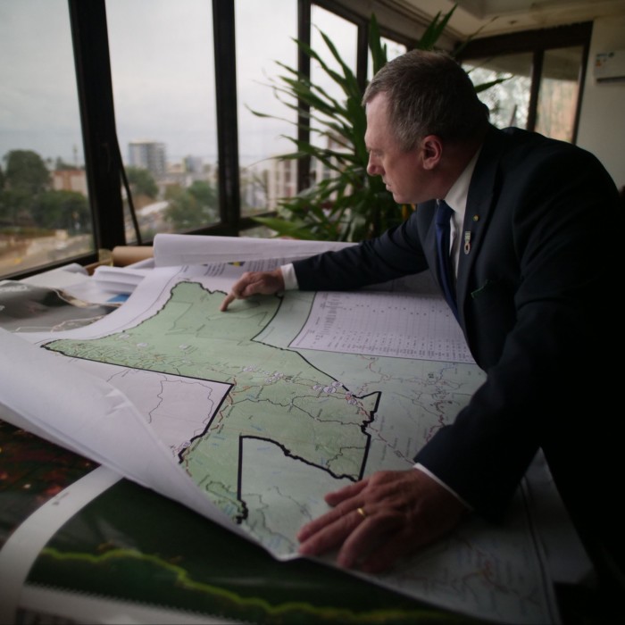 man in a dark blue suit points to an area marked on a map