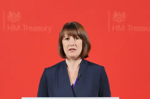 PA Media Rachel Reeves standing in front of a red background with the words HM Treasury emblazoned on