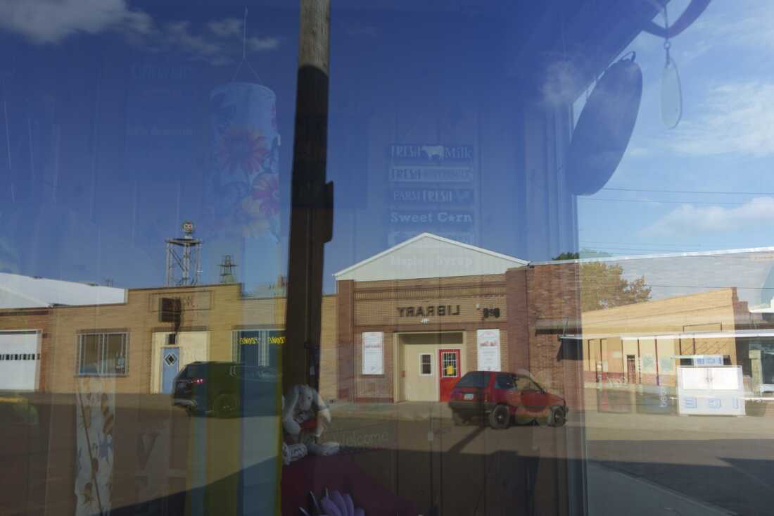 This photo shows the downtown of Glen Ullin, N.D., reflected in the window of the town's pharmacy on May 24. In the reflection is a low-slung brown brick building, a portion of which is labeled 