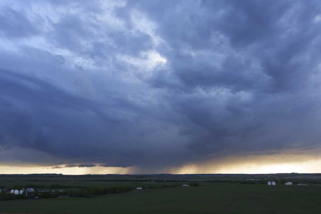 Dark rainstorm clouds skirt the horizon near Glen Ullin, N.D., on May 25. Below the clouds stretch green fields with occasional farm buildings.