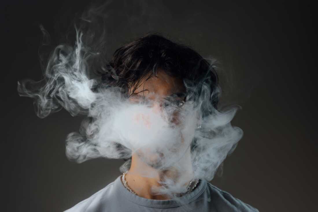 A young male behind a haze of vape smoke.