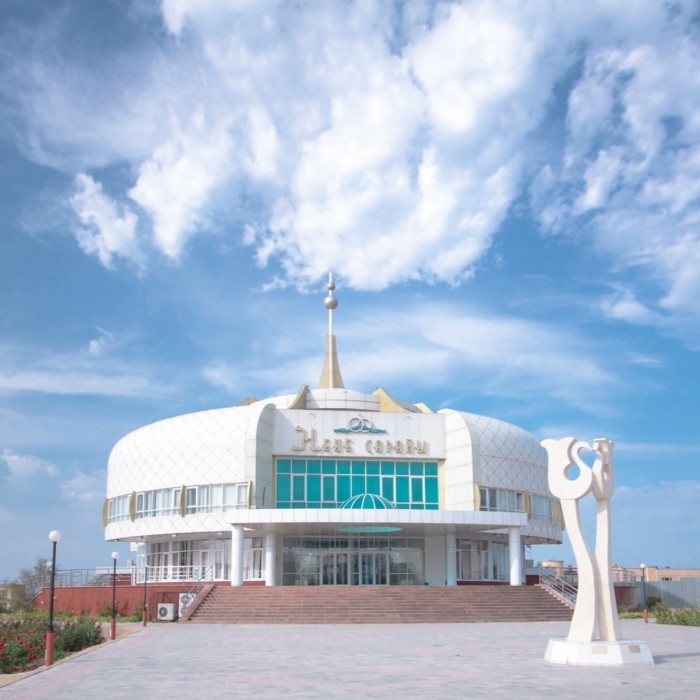 A circular modern building in white against a cloudy blue sky