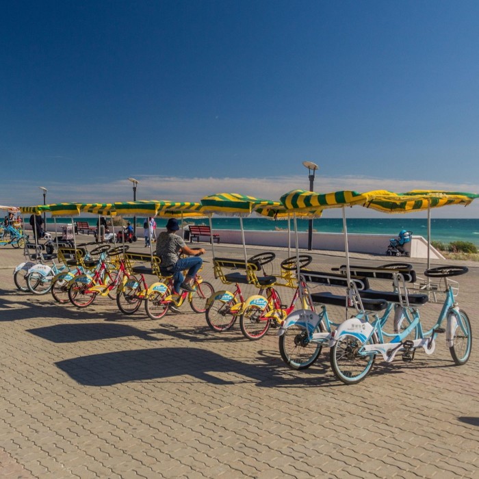 Under a deep blue sky, a row of rental bikes with stripy canopies parked on a seafront 