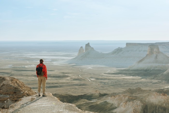 A young male tourist with a backpack on the top of a mountain gazing at a vista of mountains and desert