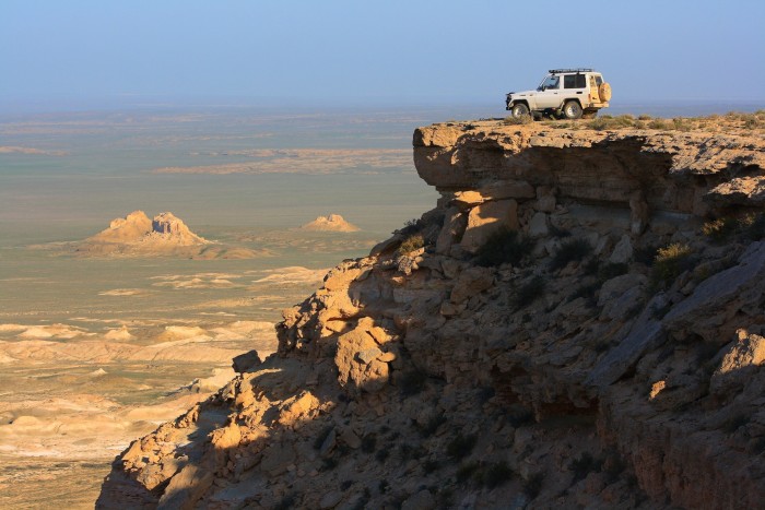 A jeep perched on top of a rocky outcrop overlooking a vista of desert