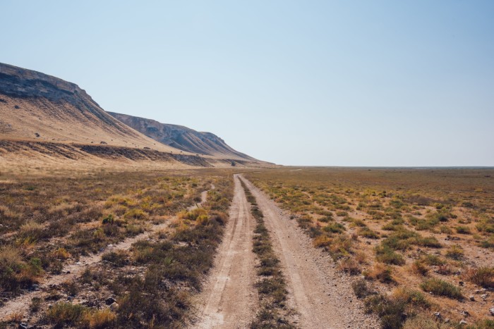 Scenery of narrow road with dry grass and rocky formations in cloudless weather 