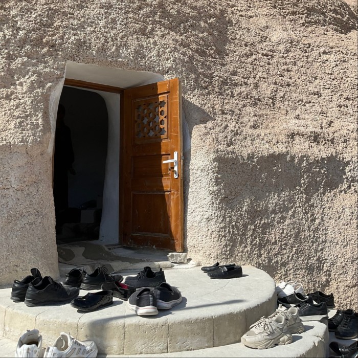 A small doorway into a shrine built in the side of a rock face. On the steps outside the door, various pairs of shoes have been left