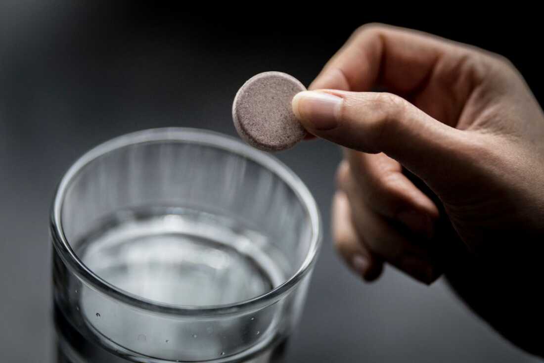 This photo shows a female hand holding an iron tablet above a glass of water.