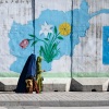 An Afghan burqa-clad woman walks past a wall mural with the map of Afghanistan, in Kabul on February 1, 2024.