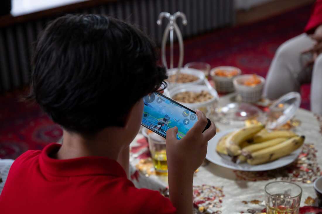 Mujib Ur Rahman plays a video game on a phone in his living room in Lewiston, Maine on Sunday, June 23, 2024.