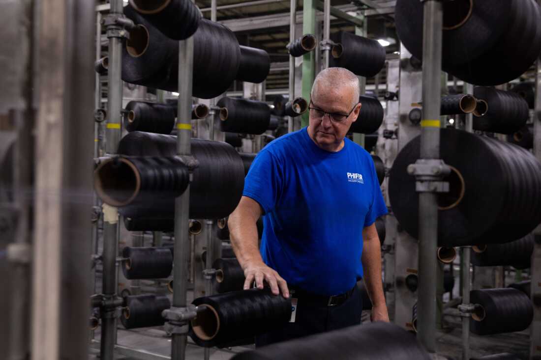 Jerry Wheat, who has worked for Phifer for 38 years, says generous health benefits make people want to work harder for the company. Wheat, a man with gray hair wearing a blue shirt, stands on the factory floor. 