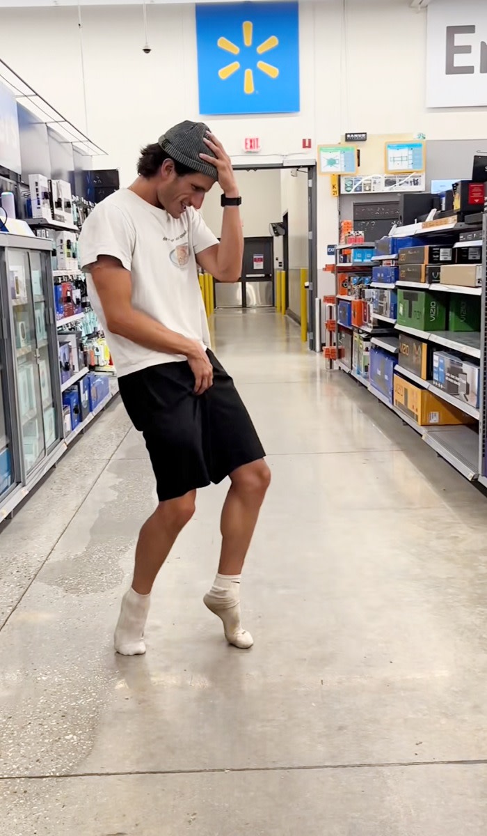 A man in shorts, t-shirt and socks dances in a store 