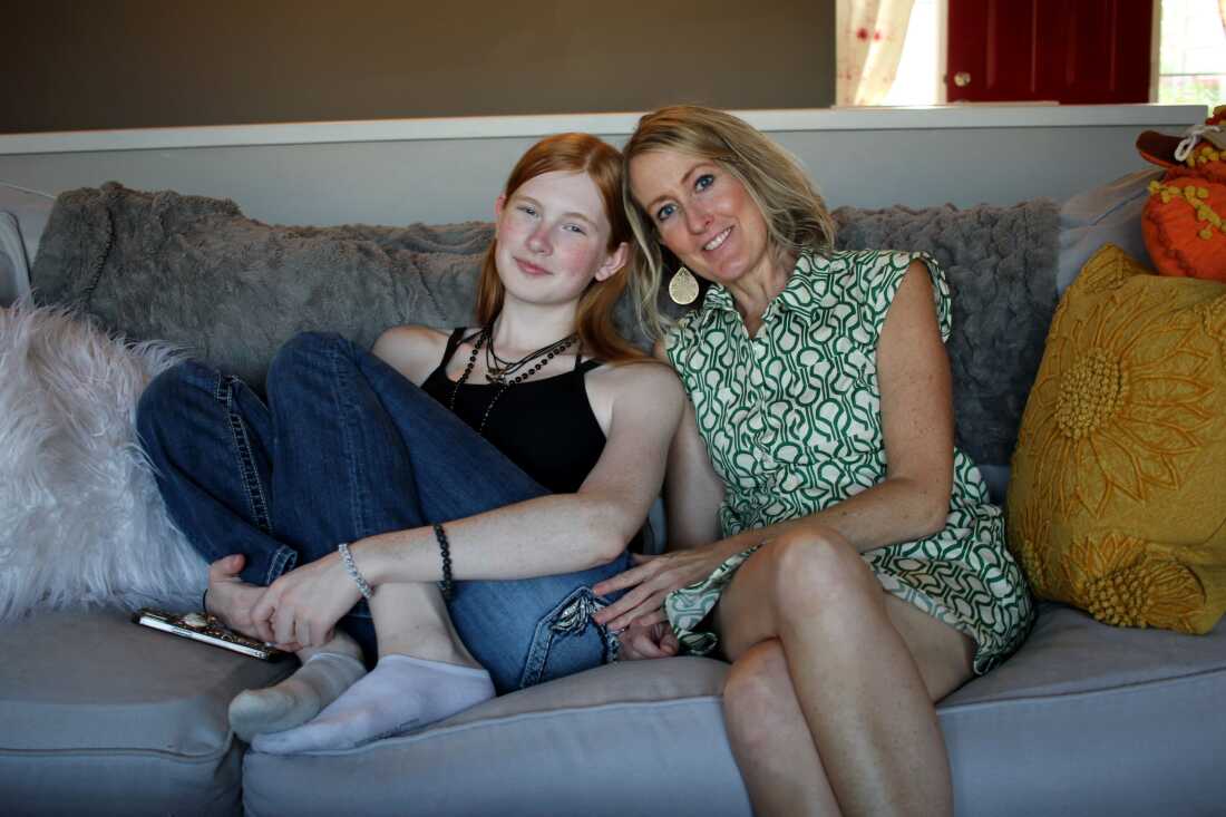 Veronica’s mom, Emily (right), says that before Veronica came out as trans, she already knew. “I was kind of just waiting to hear — I wasn't pushing it, but I just knew.” Emily has medium-length blond hair, and she is sitting close to Veronica on their couch. Veronica has her feet up on the couch and is leaning into her mom.