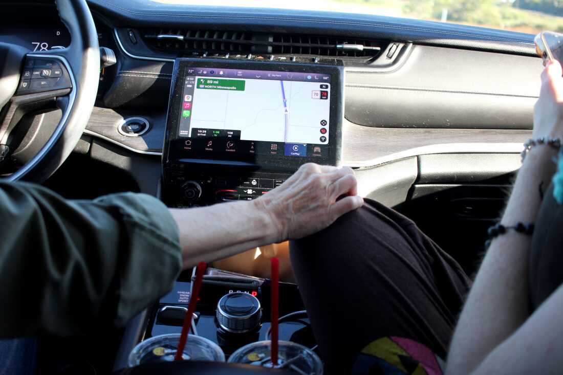 This photo is a view of the front seat of the car that Emily and Veronica are traveling in from the backseat. We see dashboard and GPS display. Mom Emily reaches over to touch Veronica's knee.