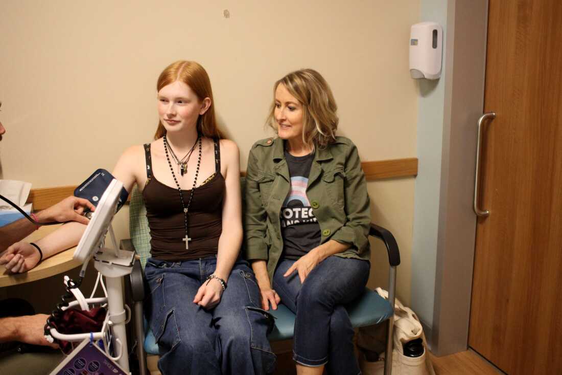 Veronica’s Minneapolis pediatrician takes her blood pressure. Emily sits next to her in the doctor's office. She's wearing a t-shirt that says 