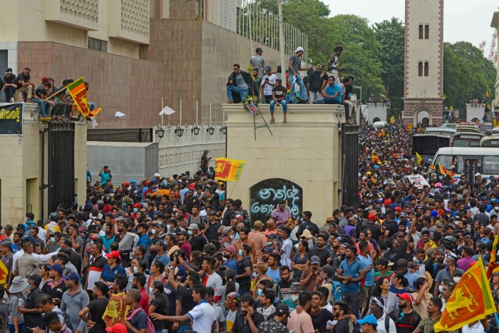 A crowd of people, some carrying with national flags and some sitting on gate posts