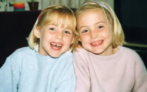 BBC/October Films A picture of Kris and Maren as young children. They have shoulder length blonde hair and are wearing pink and blue jumpers. They are smiling at the camera.