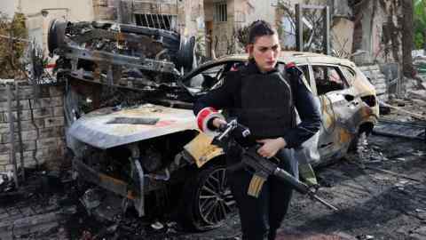 A member of the Israeli security forces, holding a rifle and wearing protective gear, stands guard in front of a cordoned-off area with a burnt-out car and significant damage in Kiryat Bialik, Haifa district, Israel, following a reported strike by Hizbollah on September 22