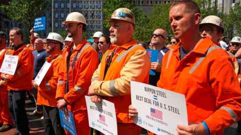 US Steel employees dressed in orange work uniforms hold signs that read "Nippon Steel = Best Deal for U.S. Steel."