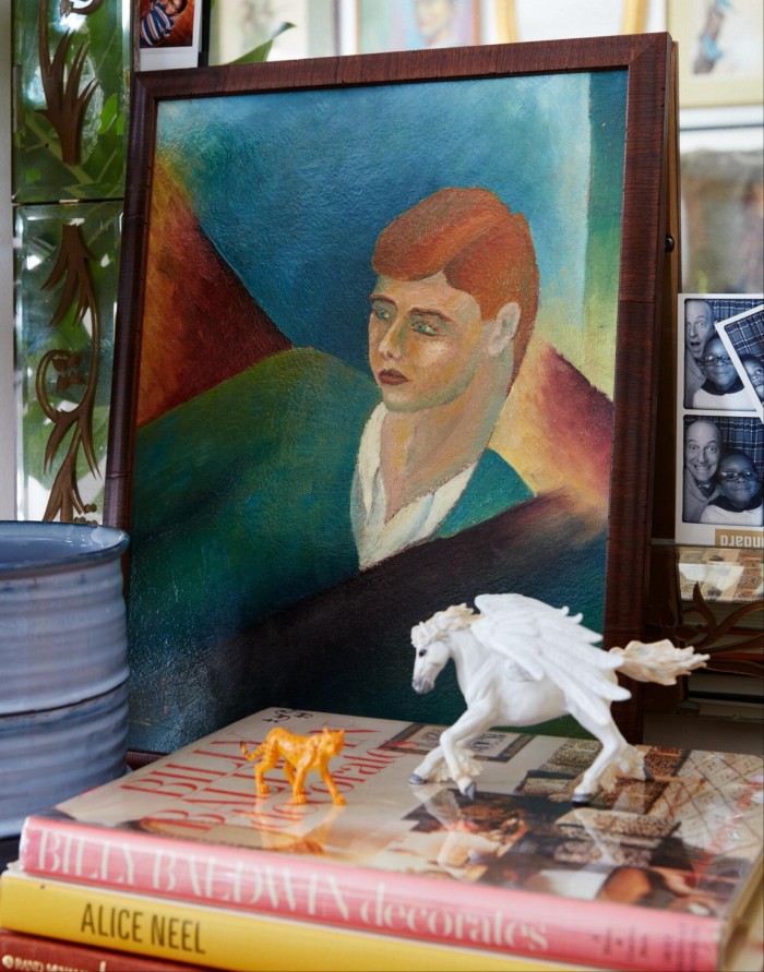 A white winged horse and tiger figurines standing on a pile of books on a table, on which is propped a painting of a boy and some photo booth portraits 